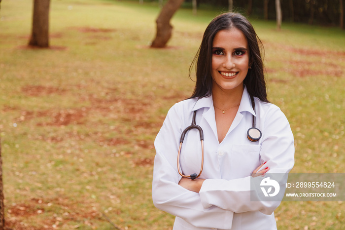 Portrait of young adult female doctor or nurse wearing lab coat and stethoscope outside.