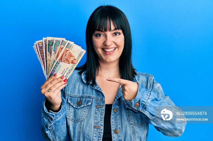 Young hispanic woman holding egyptian pounds banknotes smiling happy pointing with hand and finger