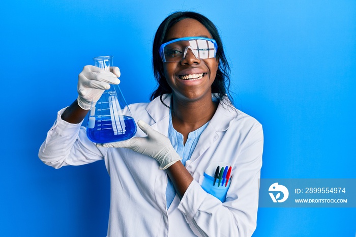 Young african american woman wearing scientist uniform holding test tube looking positive and happy standing and smiling with a confident smile showing teeth