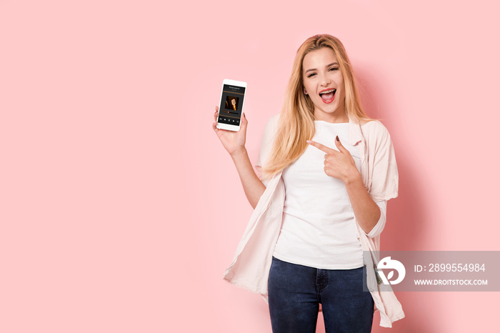 Young blonde girl is enthusiastic and points at her smartphone