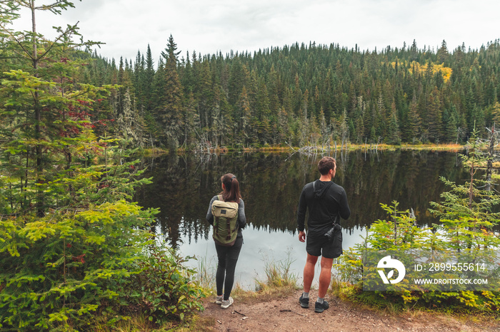 Canada travel destination outdoor activity couple tourists hiking to lake surrounded with pine trees forest. Autumn fall landscape nature.