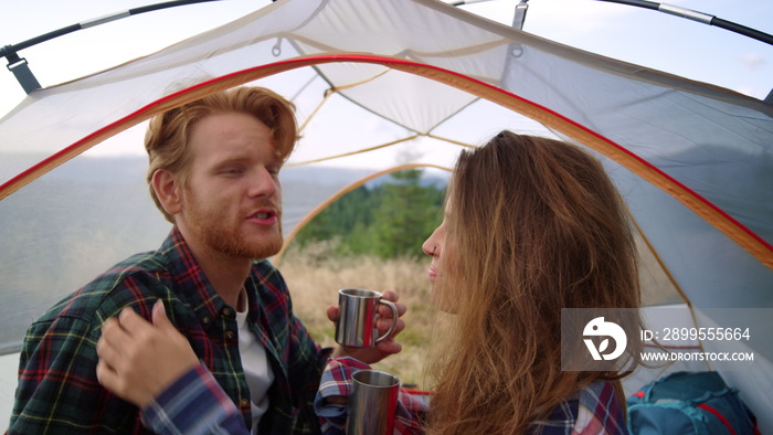 Girl taking care about guy hair in camping tent. Couple drinking tea from mugs