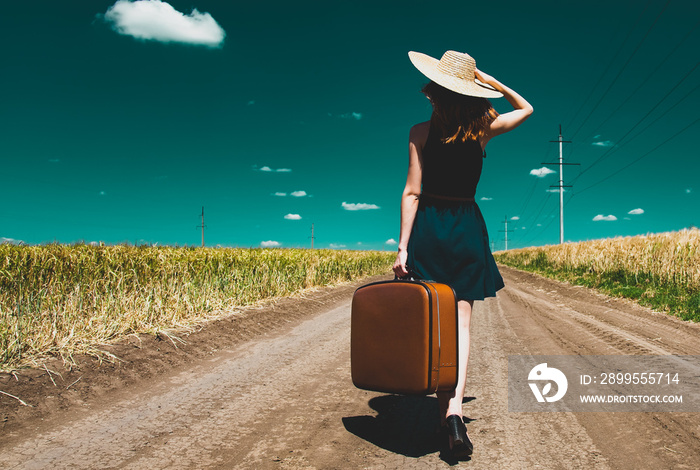 Lonely girl with suitcase at country road.