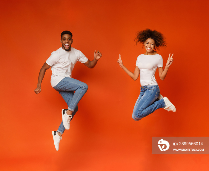 Excited black couple jumping on orange background