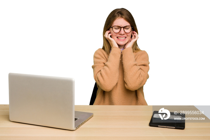 Young caucasian woman in a workplace working with a laptop isolated covering ears with hands.