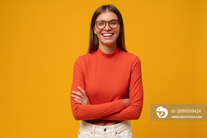 Portrait of laughing millennial woman standing with crossed hands on yellow copy space background