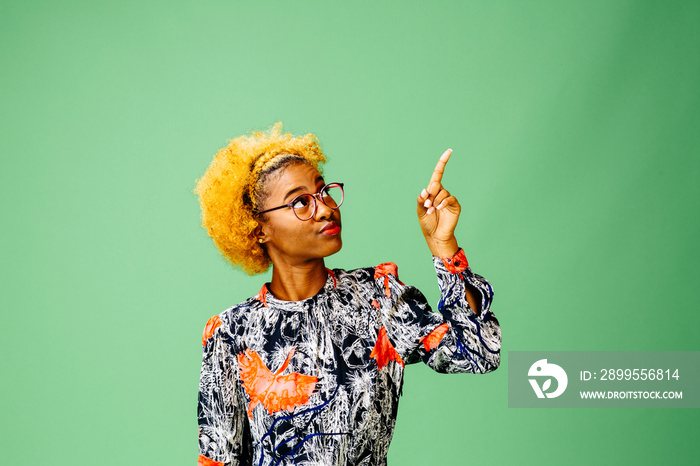 Young woman pointing up, isolated on green studio background.