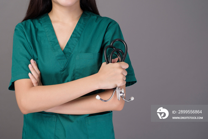 a female doctor wearing a green scrubs and stethoscope is on grey background studio