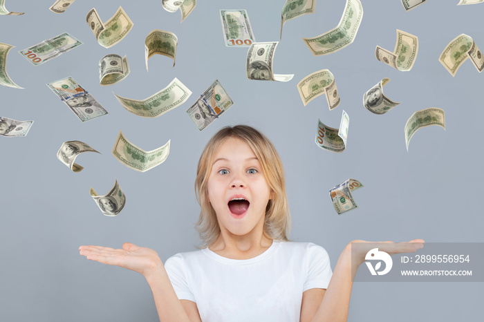 Surprised teen girl with falling us dollar money on grey background