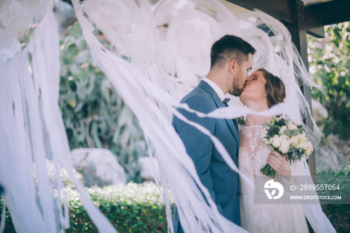 Wedding ceremony outdoors. The bride and groom kiss under a canopy decorated for the wedding