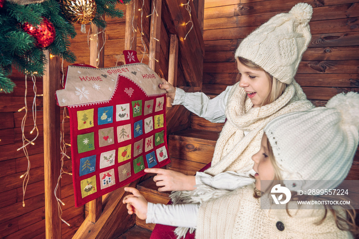 Sisters holding Christmas handmade advent calendar in a house shape