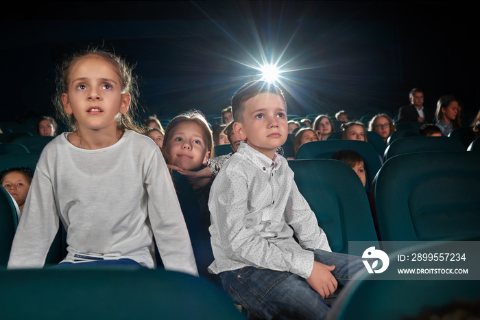 Low angle shot of little kids watching movie at the cinema looking amused and interested copyspace lens flare light childhood leisure activity people holidays carefree fascination concept.