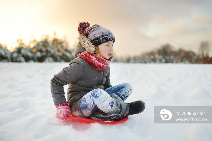 Funny little girl having fun with a sleigh in beautiful winter park. Cute child playing in a snow.