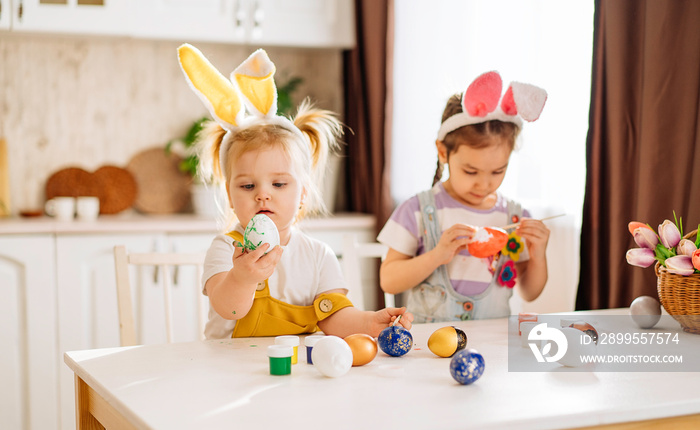 Two happy children fascinatingly draw Easter eggs in a snow-white kitchen. a girl shows an Easter egg. the concept of happiness, easter holiday for children