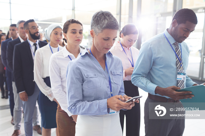 Business people standing in queue in lobby and looking files and their mobile phone