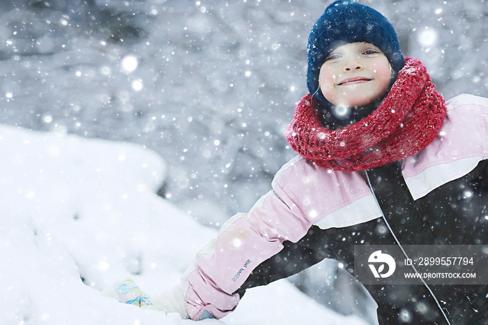 child  playing in the snow / the girl in warm sports clothes is playing with snow on a winter walk. Warm woolen hat, down jacket. Concept of a happy baby walk.