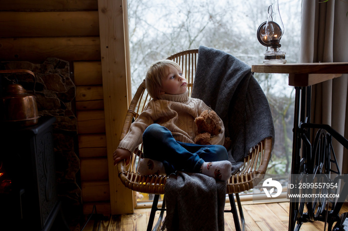 Cute toddler child in a little fancy wooden cottage, reading a book, drinking tea