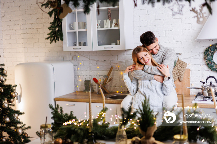 Happy young couple hugging in the kitchen decorated for the new year. New Year’s interior in the kitchen. Christmas kitchen