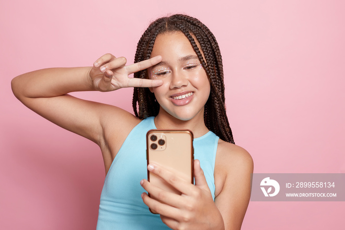 Studio shot of smiling girl with braids taking selfie