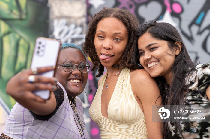 Portrait of three friends talking selfie with smart phone against graffiti wall