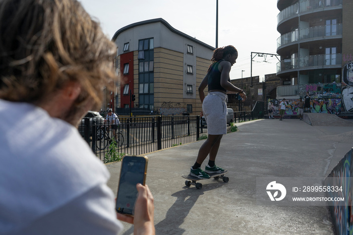 Man recording friend skateboarding in skate park