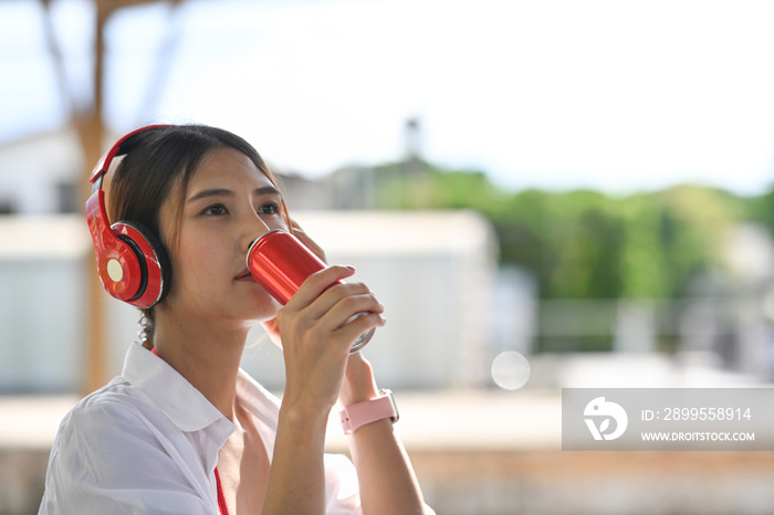 Young woman in headphone drinking soda refreshment from a can.