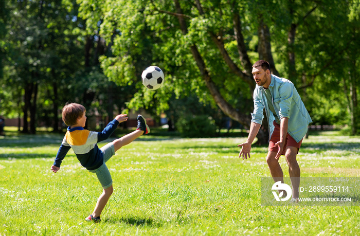 family, fatherhood and people concept - happy father and little son with ball playing soccer at summer park