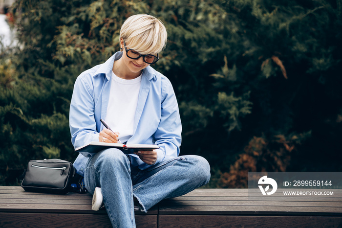 Young woman sitting on bench and writing in a notebook