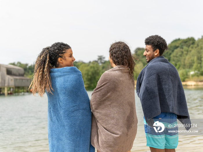 Friends wrapped in towels standing by lake