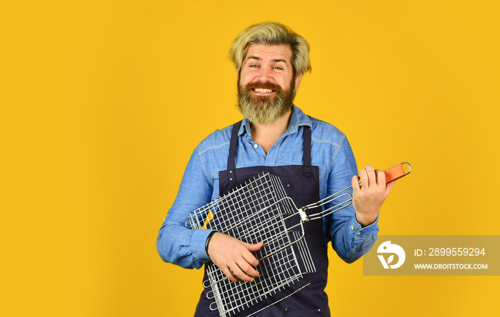 Tools for roasting meat. Man in apron hold barbecue grill. Chef cooking bbq food. Culinary concept. Cooking utensils. Summer picnic. Hipster dyed beard promoting bbq equipment. Cooking healthy