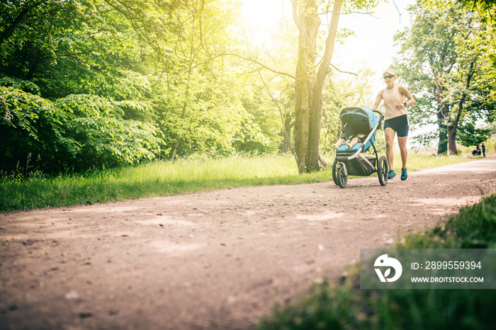 Running woman with baby stroller enjoying summer in park