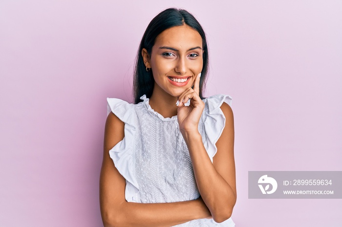 Young brunette woman wearing elegant summer shirt smiling looking confident at the camera with crossed arms and hand on chin. thinking positive.