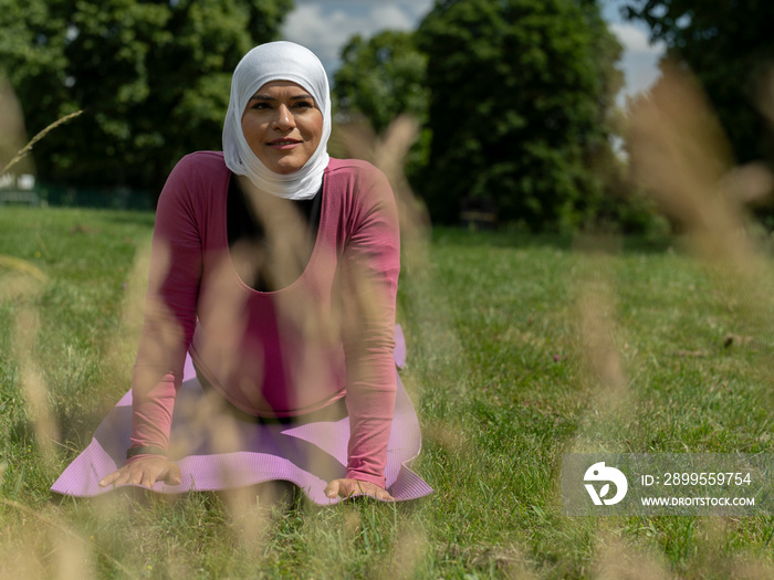 UK,Sutton,Portrait of woman in headscarf practicing yoga in grassy field