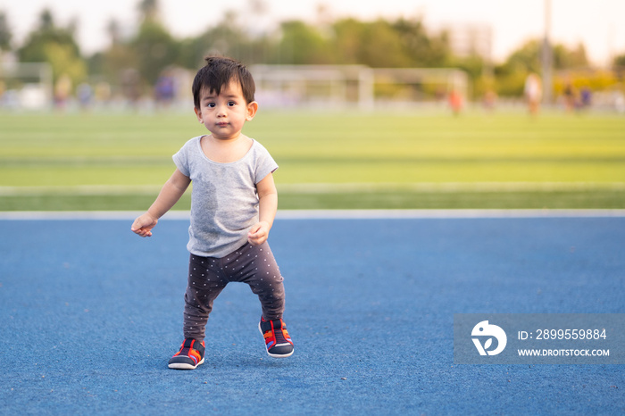 A little toddler boy is trying for independent first step in the stadium, concept of learning and developing of child in the first year of life and outdoor learning activity for kid development.