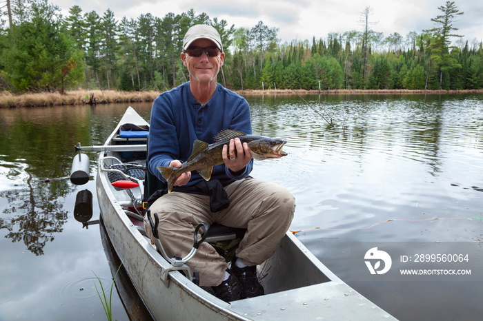 Smiling fisherman sitting in a canoe on a Minnesota lake holds up a walleye