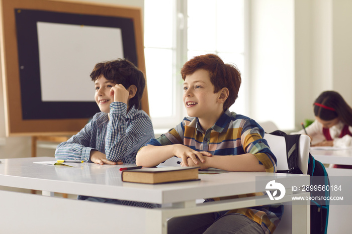 Pupils studying at desks in classroom. Portrait of two elementary school boys sitting in class and listening to the teacher. Concept of interesting school lessons for children.