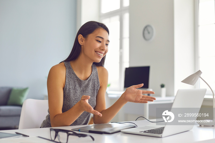 Happy young Asian woman sitting at desk at home and using laptop computer for video call