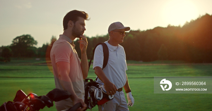 Rich men playing golf on sunset summer course. Two players enjoy sport on field.