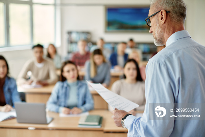 University professor reads from paper while giving lecture to his students in the classroom.