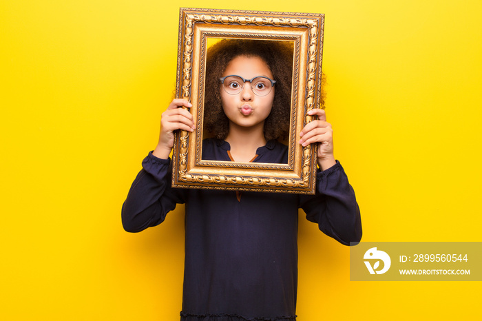 african american little girl  against flat wall holding a baroque frame