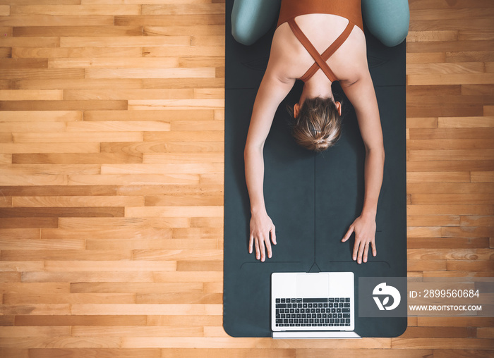 Top view of woman practicing yoga on yoga mat with laptop.
