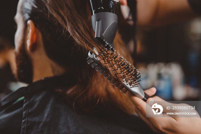 Barber makes hair styling to man with hairdryer and comb