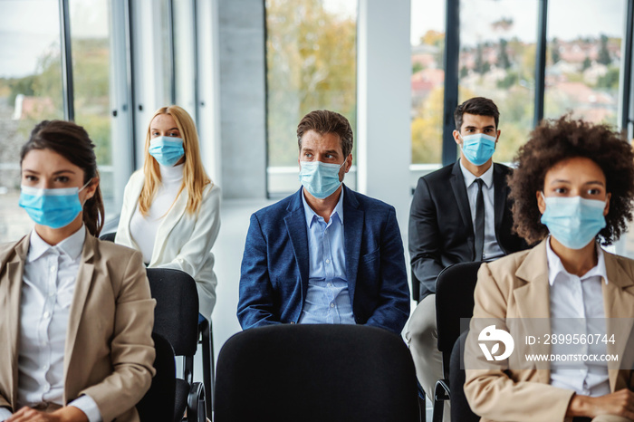 Multiracial group of business people with face masks sitting on seminar during corona virus.