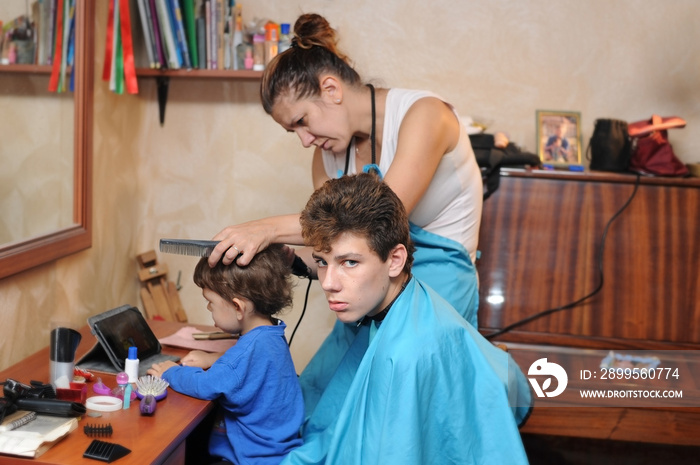 A woman works as a hairdresser at home. She cuts hair her sons with a special hairdresser’s model