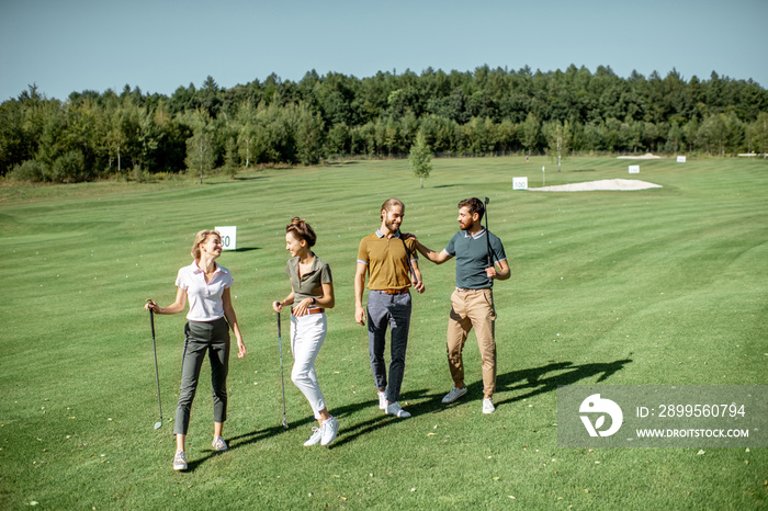 Group of friends talking and walking with putters during the golf play on the beautiful course on a sunny day