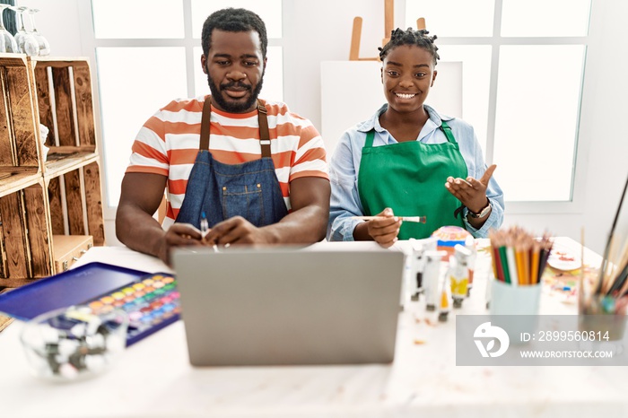 African american painter couple smiling happy having online paint class sitting on the table at art studio.