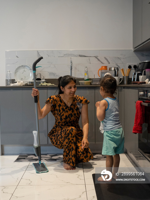 Young woman mopping floor while son (2-3) watching