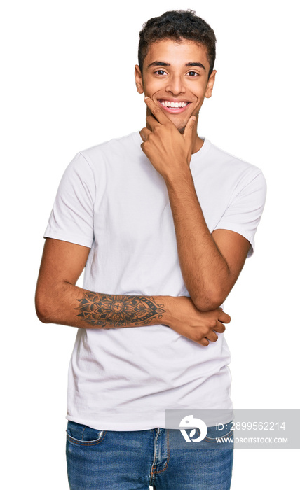 Young handsome african american man wearing casual white tshirt looking confident at the camera smiling with crossed arms and hand raised on chin. thinking positive.