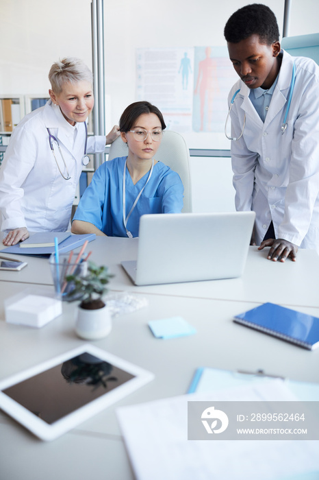 Multi-ethnic group of doctors using computer while working on medical project together, copy space