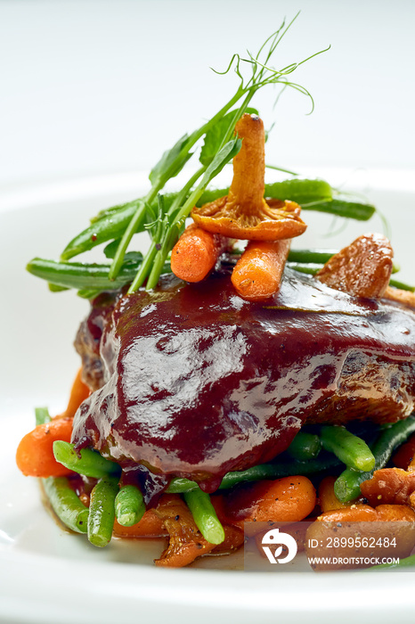 Beef cheek steak, caramelized in wine sauce with chanterelles and asparagus in a white plate. Isolated on grey background.